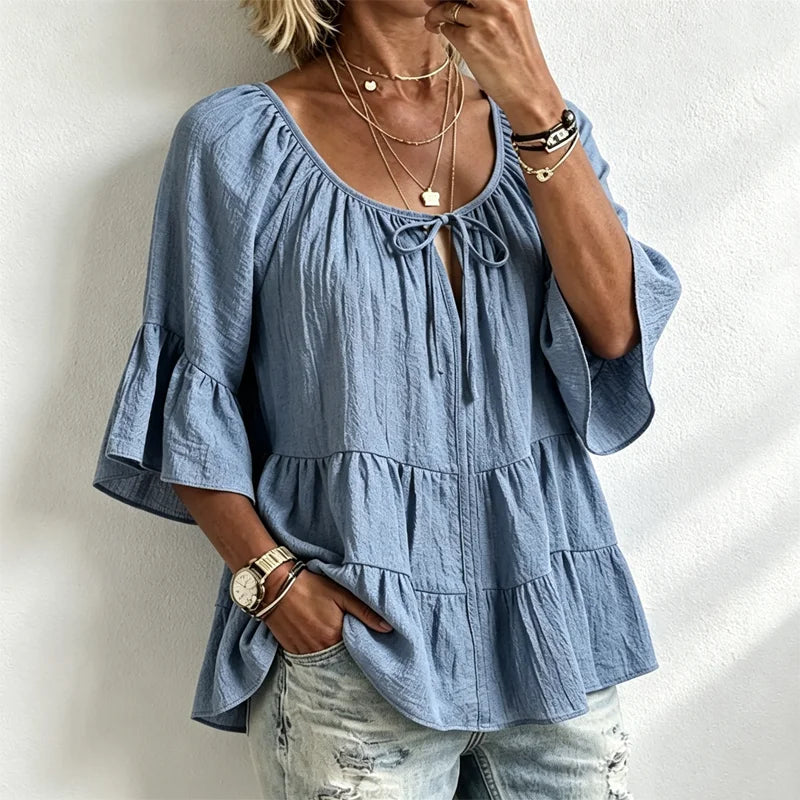 Elegancka damska bluzka z falbankami i wiązaniem przy dekolcie, rękawami 3/4 typu dzwon, o fakturze materiału i w stylu boho-chic, w swobodnym fasonie z baskinką.