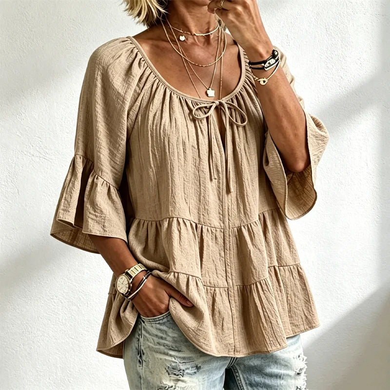 Elegancka damska bluzka z falbankami i wiązaniem przy dekolcie, rękawami 3/4 typu dzwon, o fakturze materiału i w stylu boho-chic, w swobodnym fasonie z baskinką.