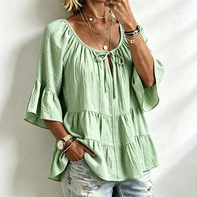 Elegancka damska bluzka z falbankami i wiązaniem przy dekolcie, rękawami 3/4 typu dzwon, o fakturze materiału i w stylu boho-chic, w swobodnym fasonie z baskinką.