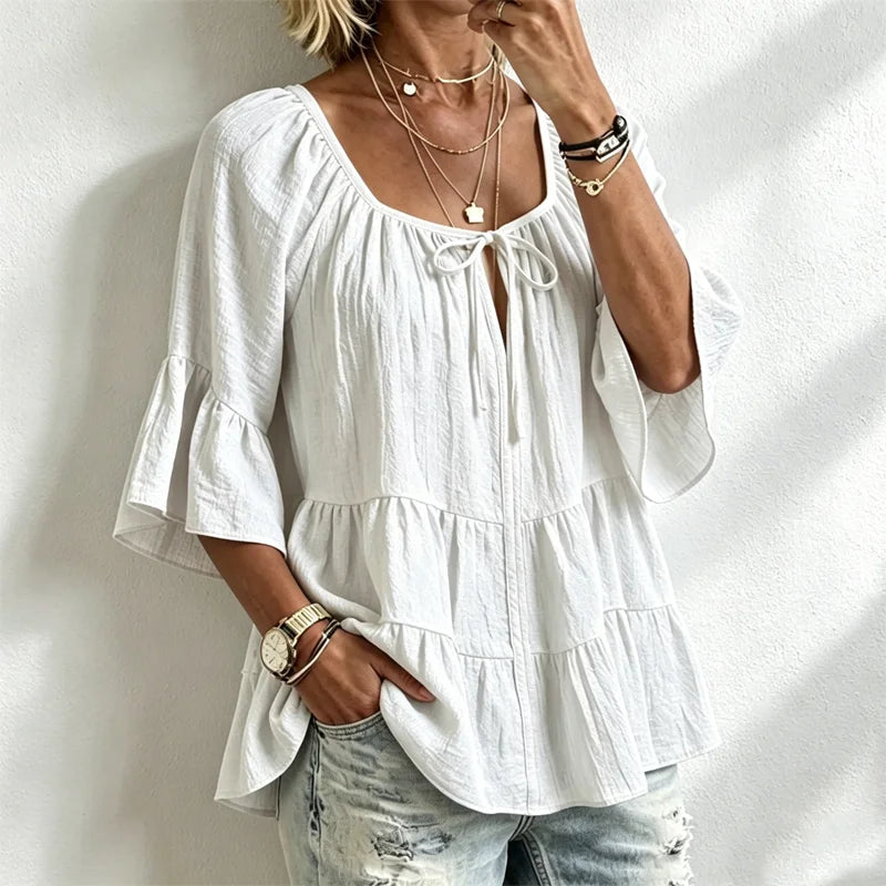 Elegancka damska bluzka z falbankami i wiązaniem przy dekolcie, rękawami 3/4 typu dzwon, o fakturze materiału i w stylu boho-chic, w swobodnym fasonie z baskinką.