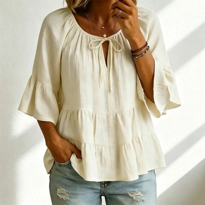 Elegancka damska bluzka z falbankami i wiązaniem przy dekolcie, rękawami 3/4 typu dzwon, o fakturze materiału i w stylu boho-chic, w swobodnym fasonie z baskinką.
