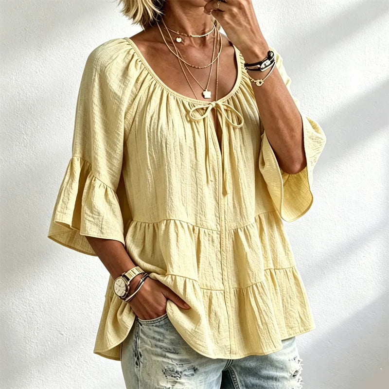 Elegancka damska bluzka z falbankami i wiązaniem przy dekolcie, rękawami 3/4 typu dzwon, o fakturze materiału i w stylu boho-chic, w swobodnym fasonie z baskinką.