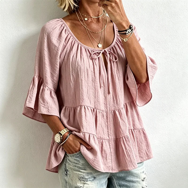 Elegancka damska bluzka z falbankami i wiązaniem przy dekolcie, rękawami 3/4 typu dzwon, o fakturze materiału i w stylu boho-chic, w swobodnym fasonie z baskinką.